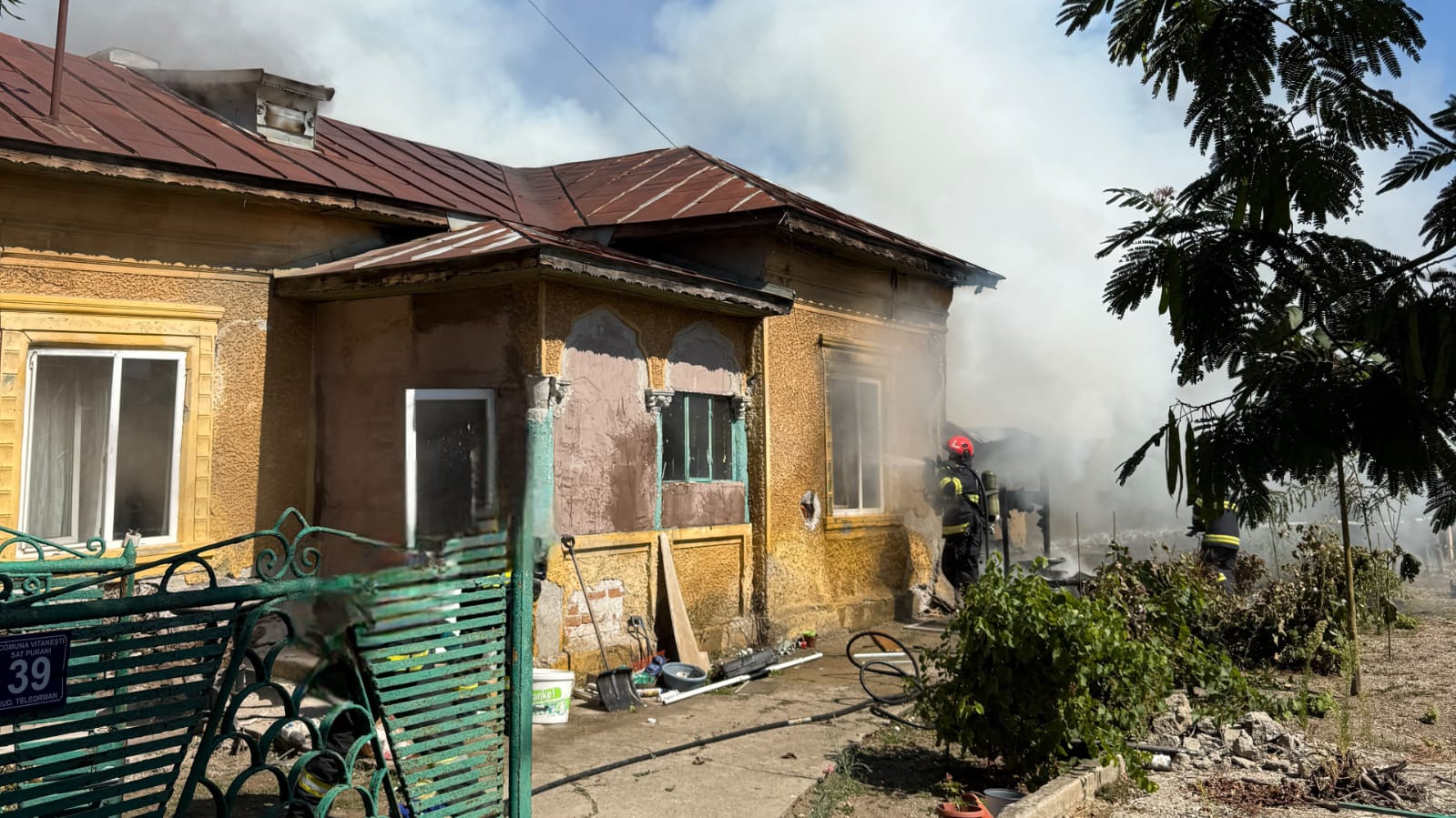 Pompieri intervenind lângă casa cuprinsă de fum din Purani